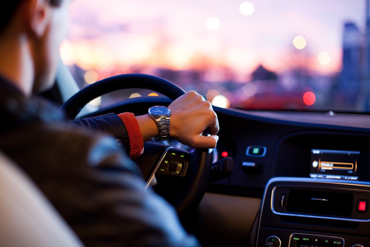 Fahrzeugdaten im Connected Car: Fahrer am Lenkrad vor beleuchtetem Cockpit mit Infotainment-Display