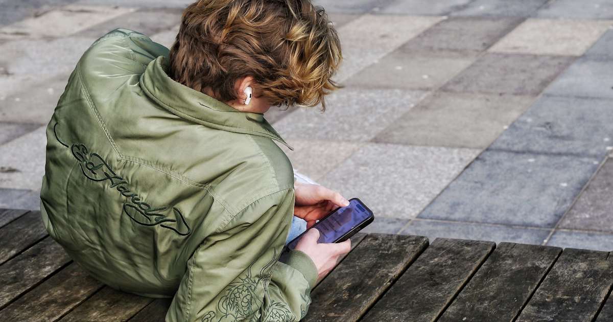TikTok und Instagram im WLAN sperren: Jugendlicher mit Kopfhörer schaut auf sein Smartphone